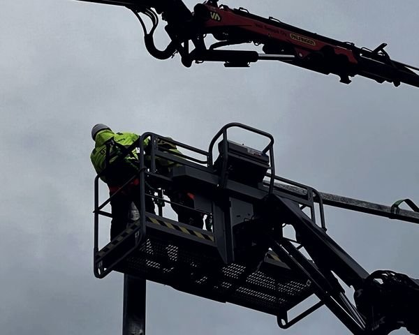 Asentaja henkilönostimen korissa, taustalla nosturin puomi.